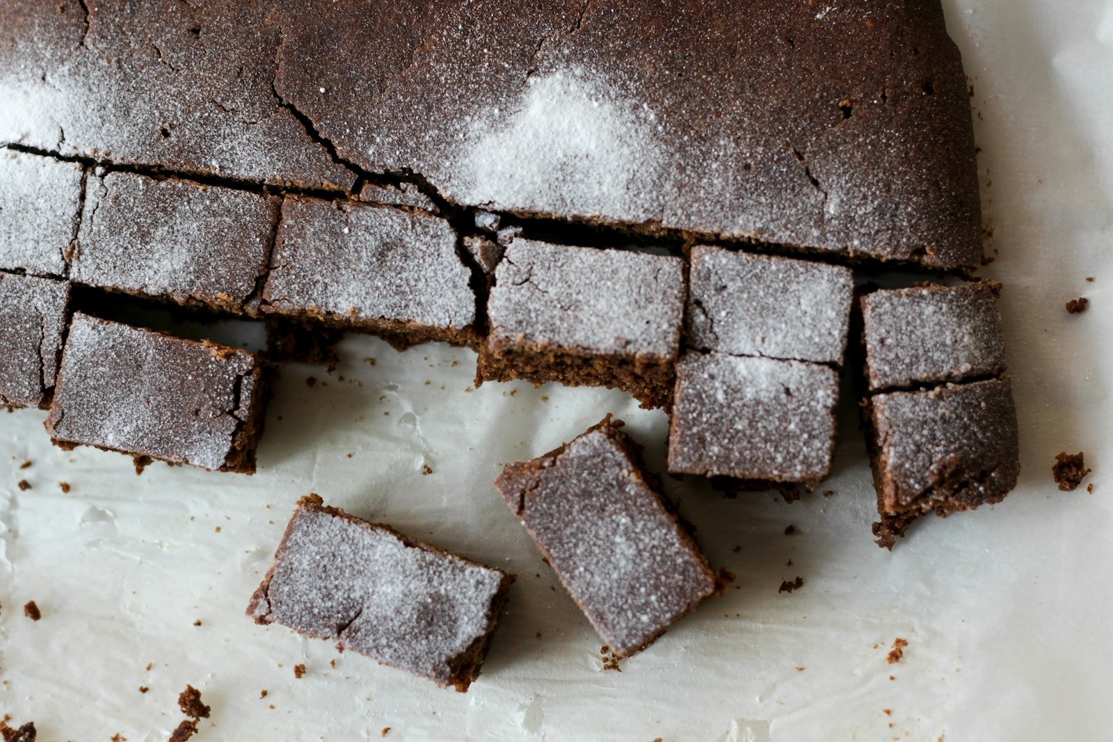 Dark spiced gingerbread squares dusted with powdered sugar on parchment paper