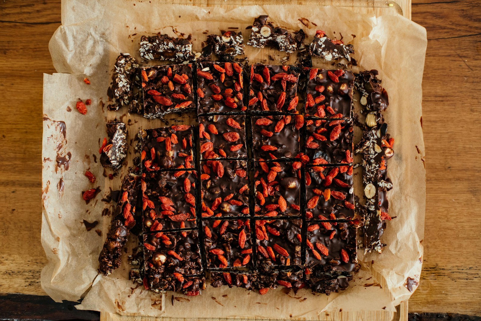 Dark chocolate fruit and nut bars with red dried berries cut into squares on parchment