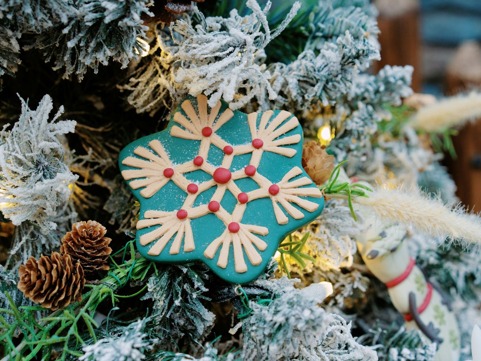 Teal snowflake ornament cookie hanging on a frosted Christmas tree