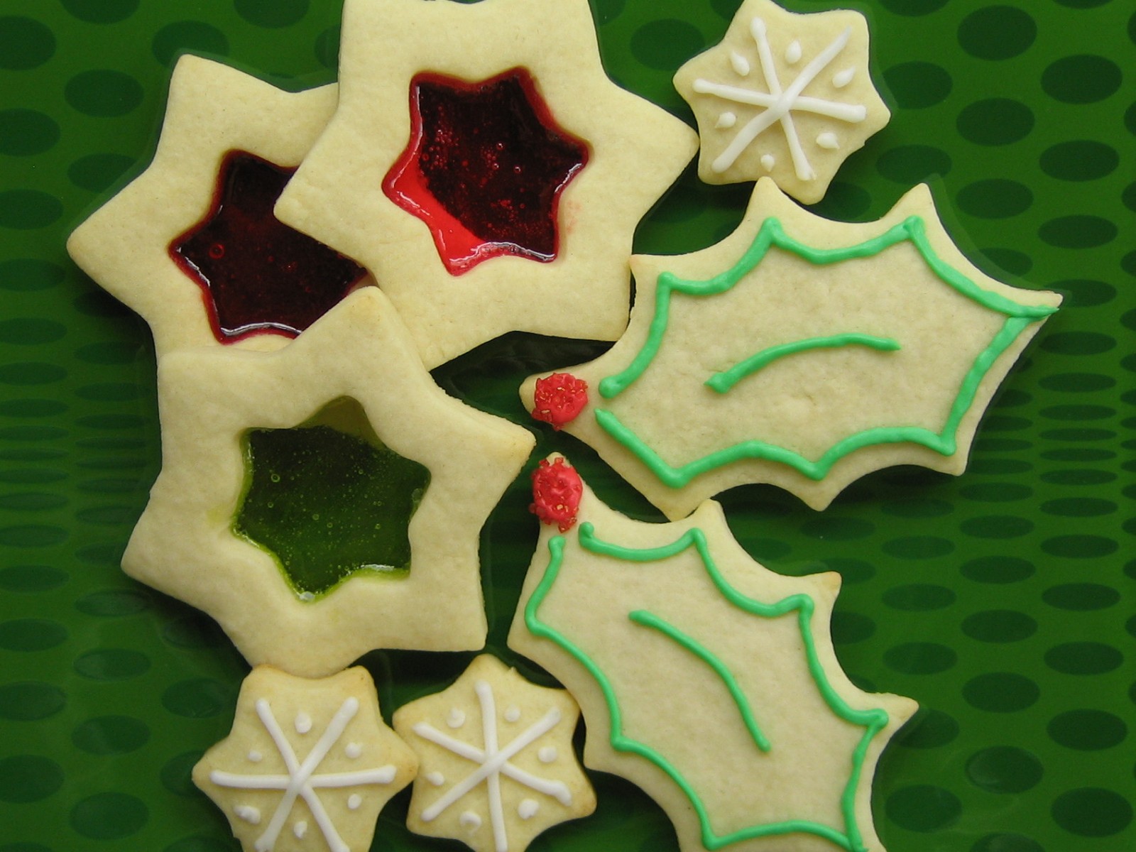 Stained glass showstopper Christmas cookies with melted red and green candy centers next to holly leaves
