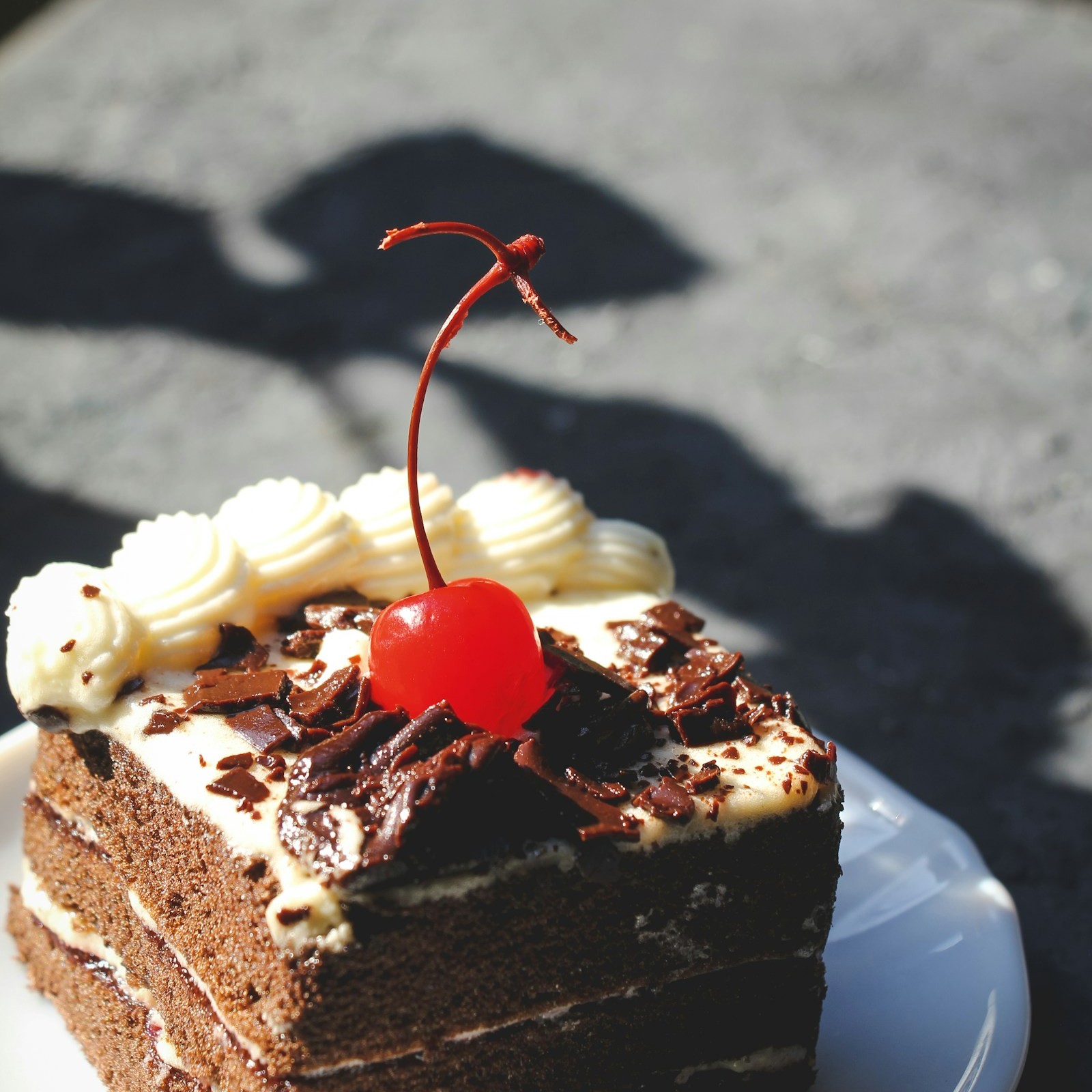 Square of layered chocolate sheet cake with whipped cream, chocolate shavings and a cherry