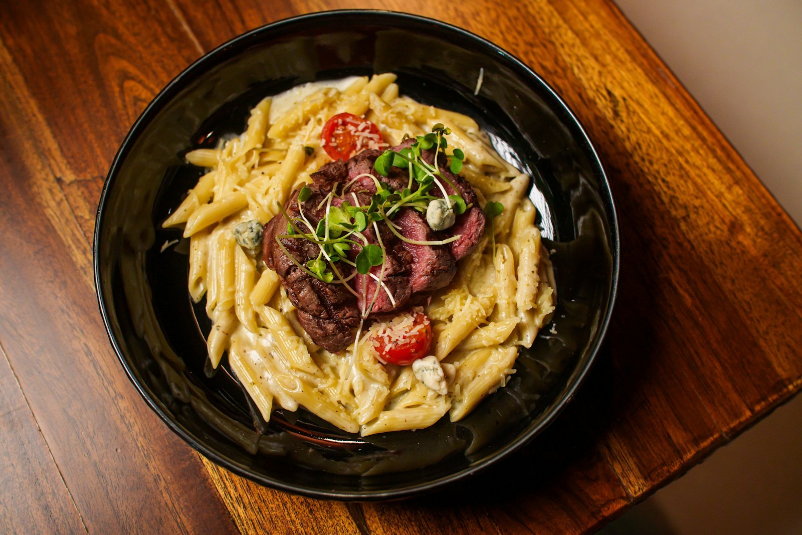 Sliced beef over creamy noodles in a dark bowl