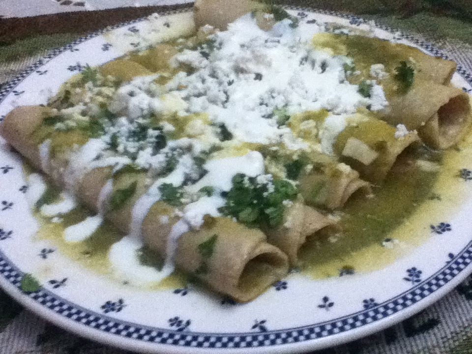 Green enchiladas topped with cream and crumbled cheese