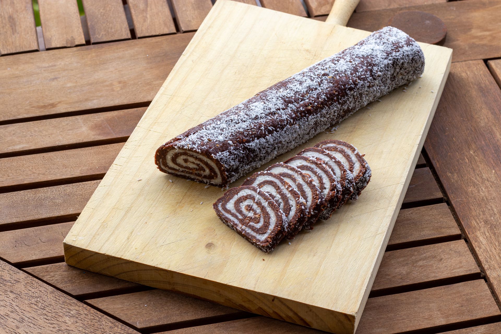 Sliced chocolate cake roll with cream filling on a wooden board