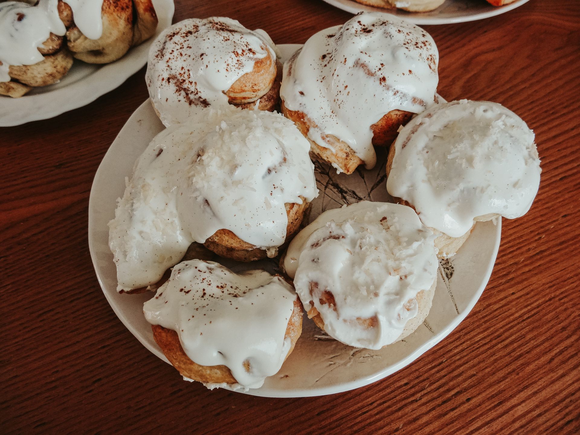 Buns covered in thick white cream cheese icing on a plate