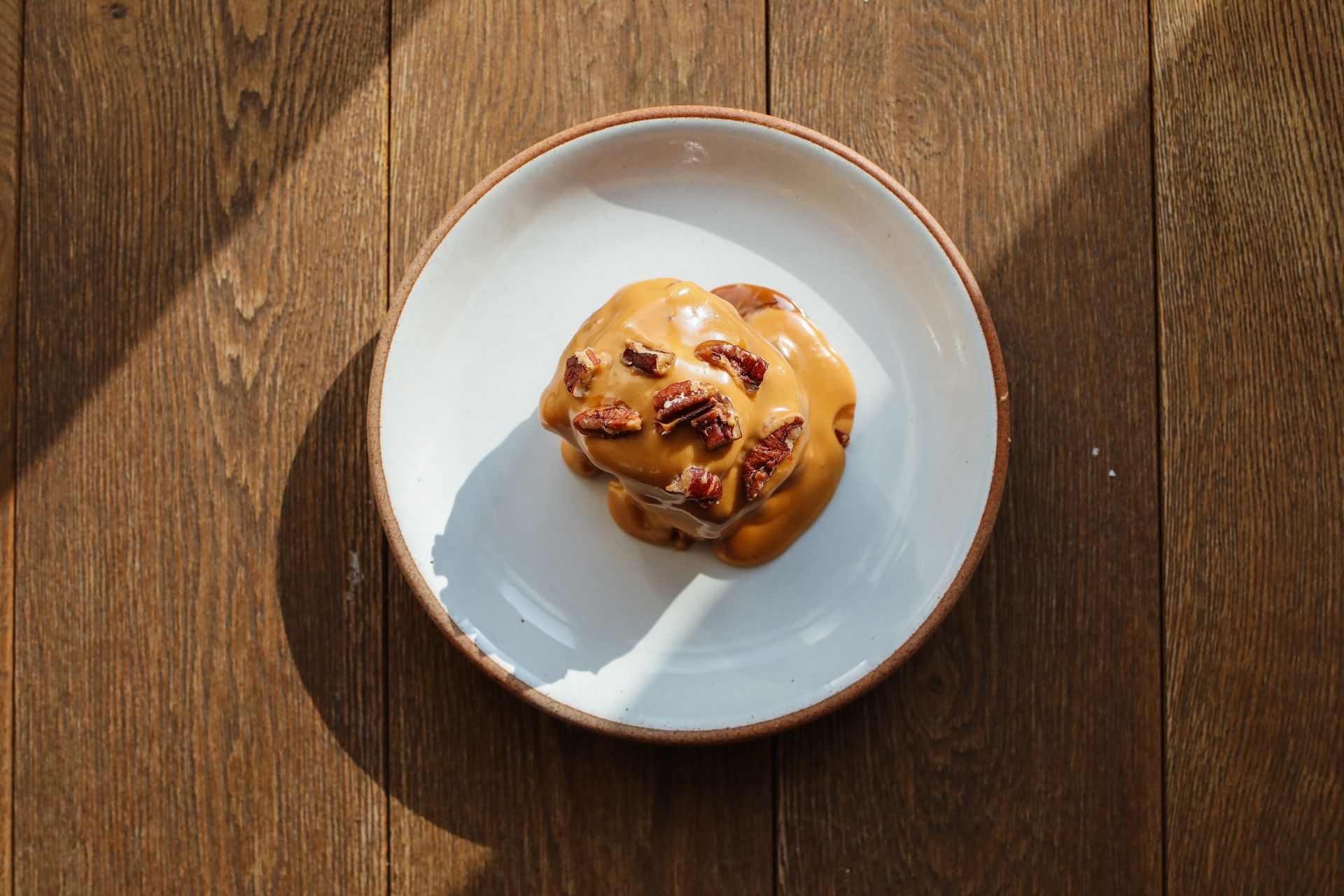 Caramel covered bun with pecans on a white plate