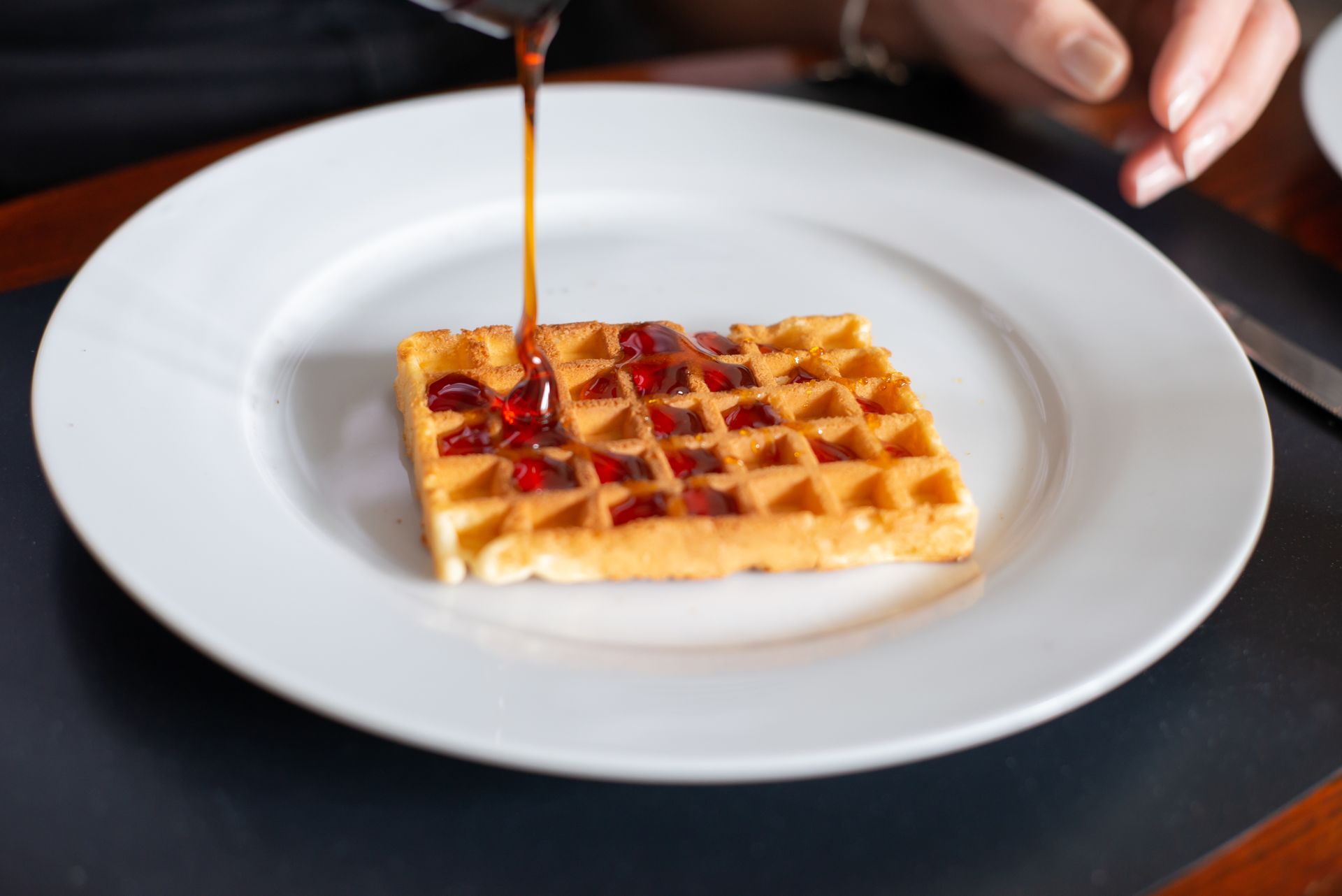 Golden waffle on a white plate with syrup being poured over