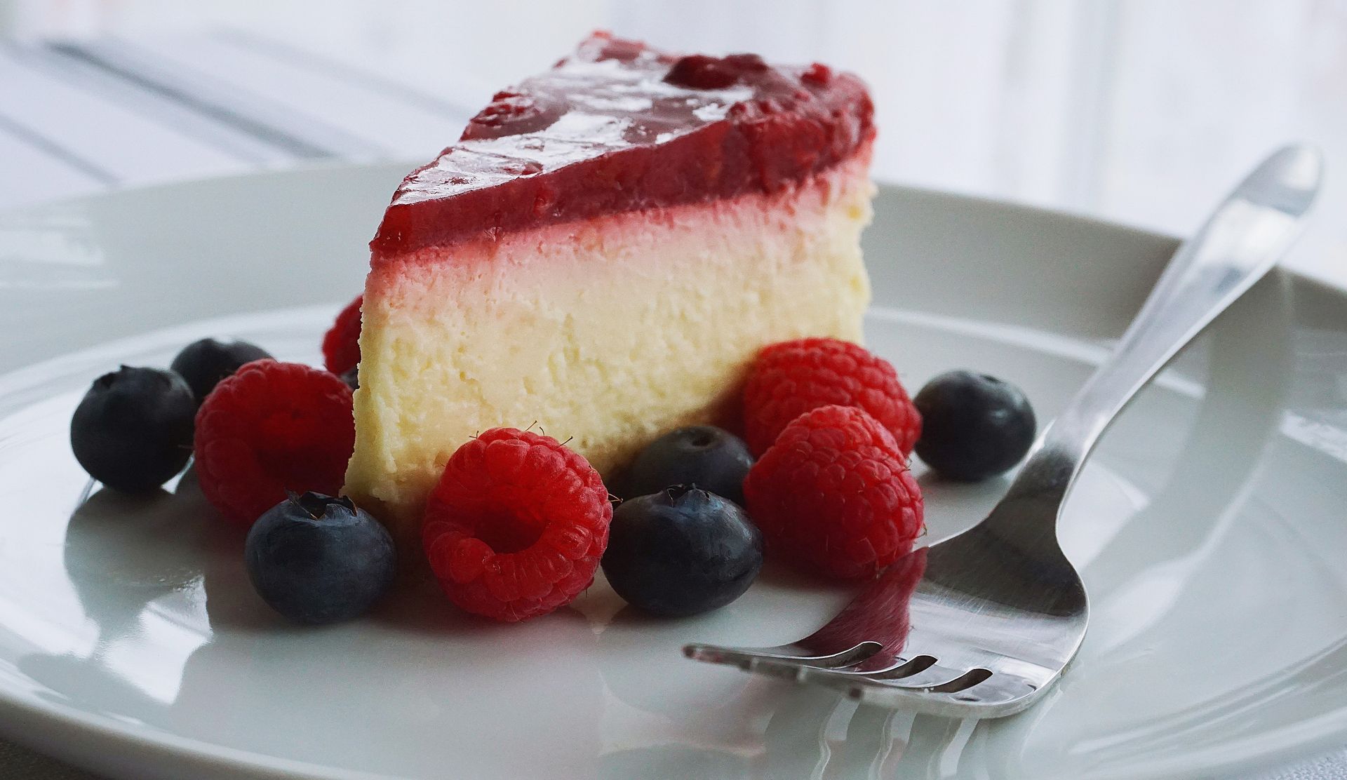 Cheesecake slice topped with berry sauce and fresh raspberries