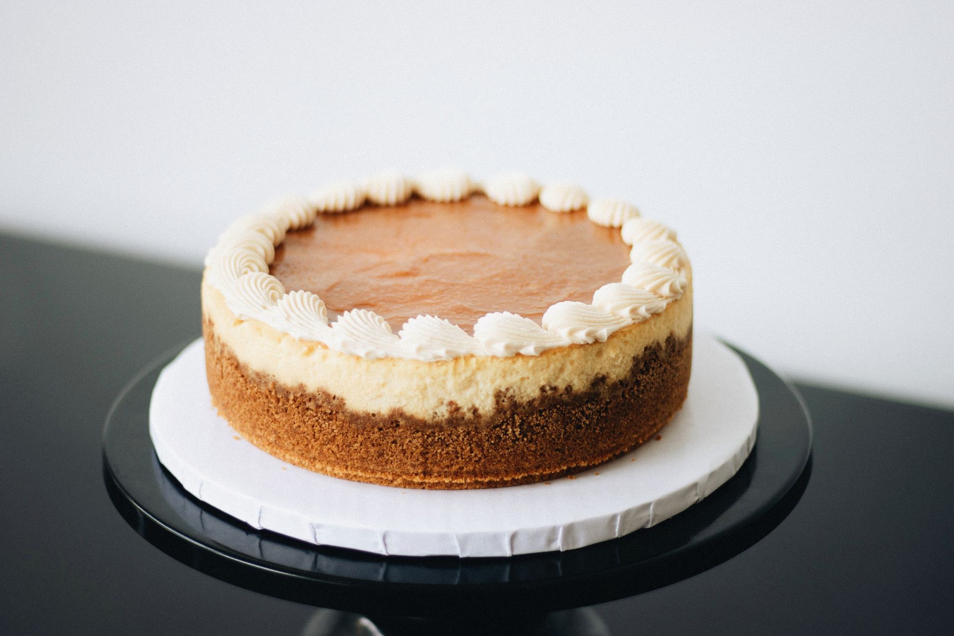 A whole creamy holiday dessert with a whipped cream border on a black cake stand