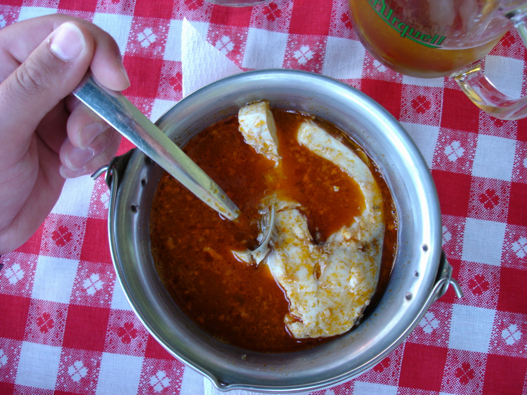 Red Hungarian fish soup in a metal pot on a checkered tablecloth