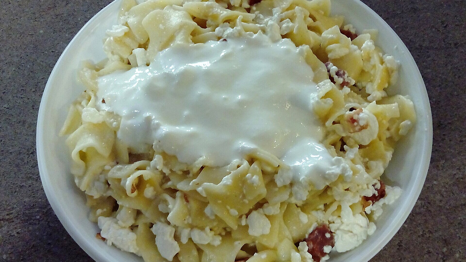 Hungarian recipes: noodles topped with cottage cheese and sour cream in a white bowl