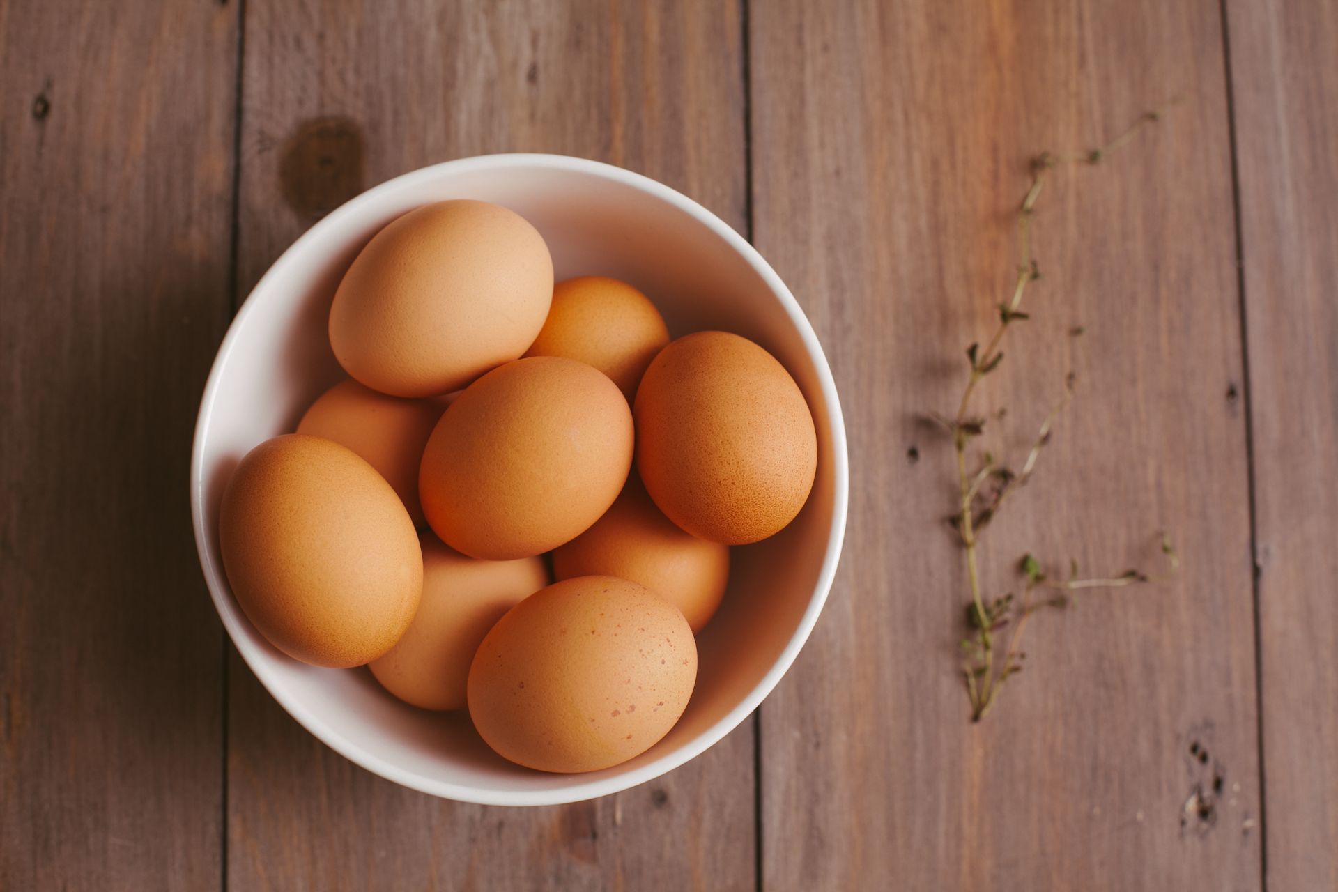 Fresh brown eggs in a white bowl on a wooden table