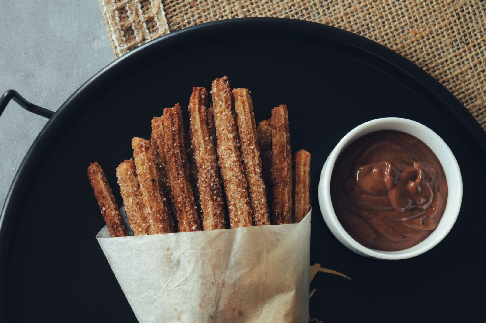 Cinnamon sugar churro sticks in a paper cone with chocolate dip