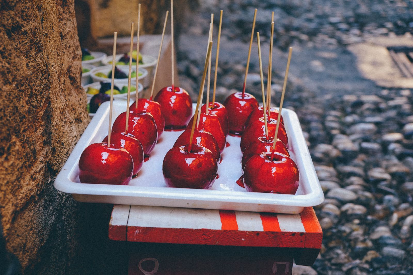 Shiny red candy apples on sticks on a white tray, homemade Halloween candy