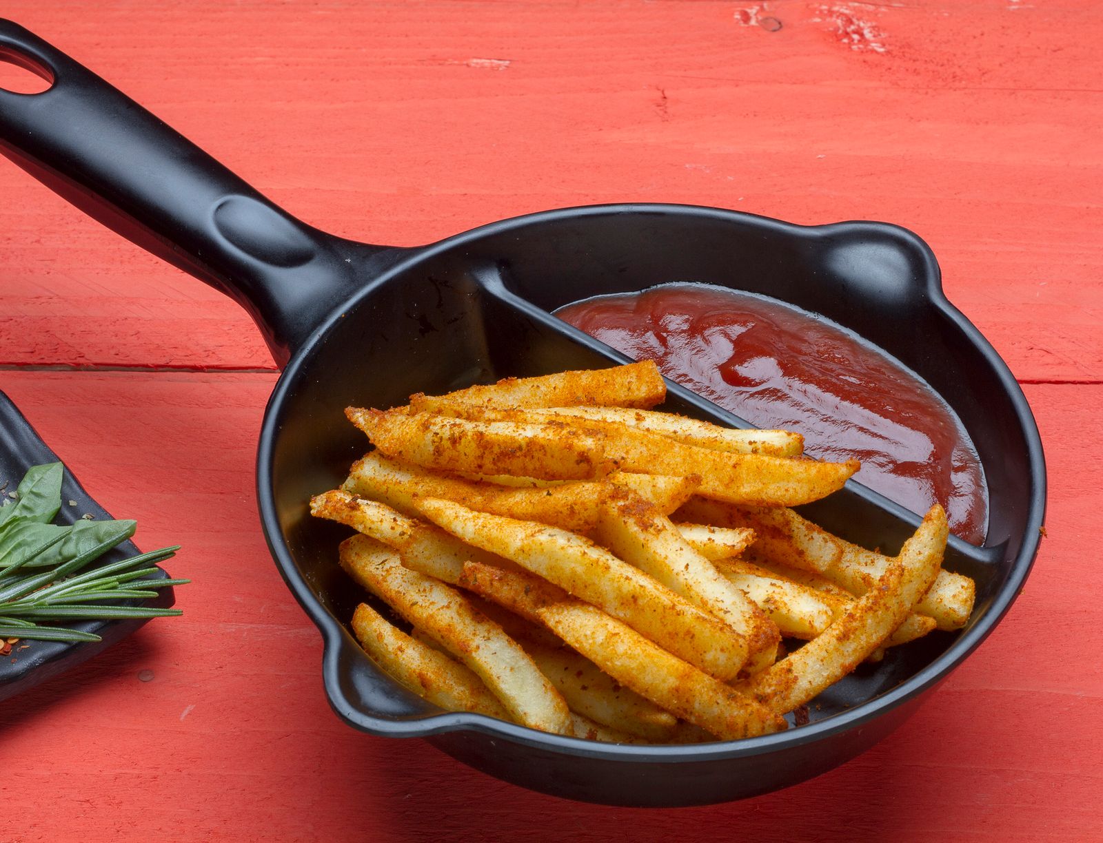 Seasoned potato sticks with ketchup in a black skillet