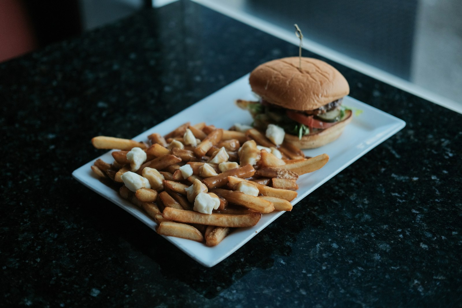 Poutine with gravy and cheese curds on a plate beside a burger