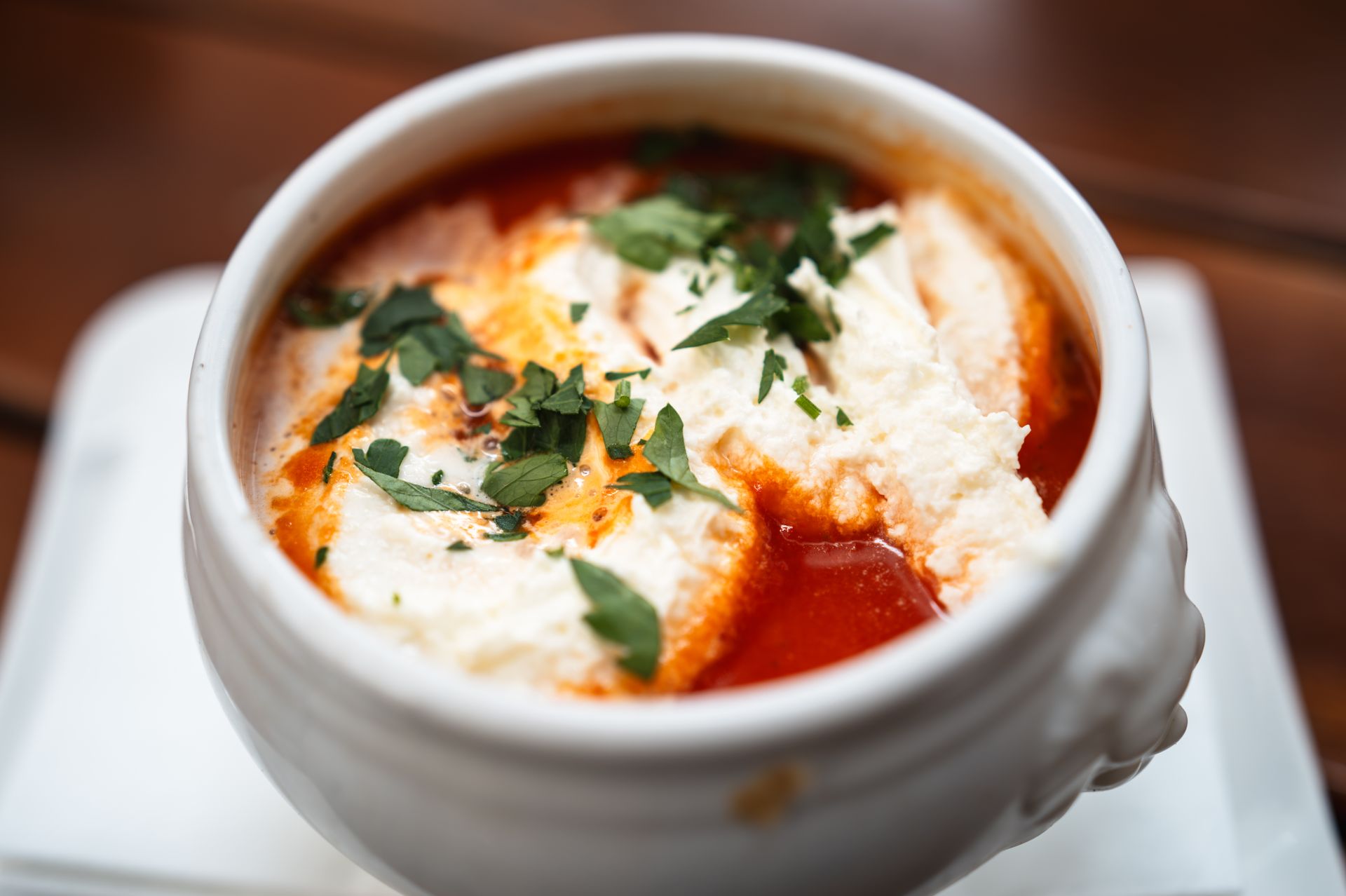 Creamy cheese dollop and fresh herbs on a bowl of tomato broth