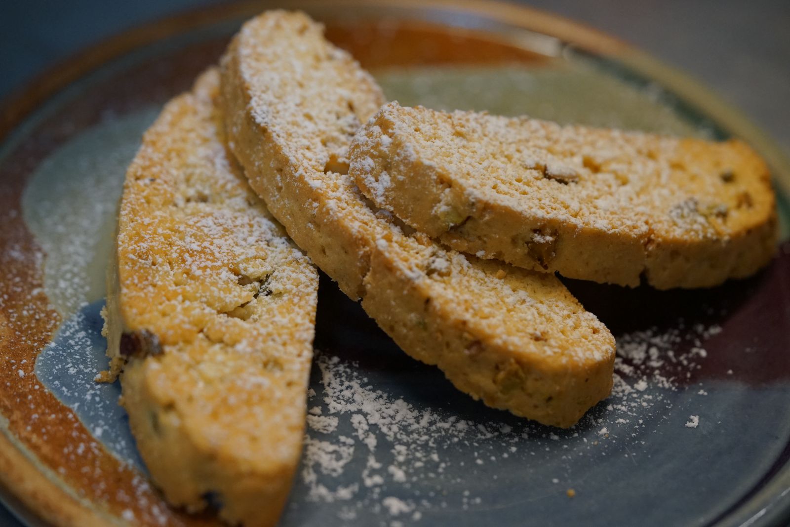 Twice-baked cookies dusted with powdered sugar on a dark plate