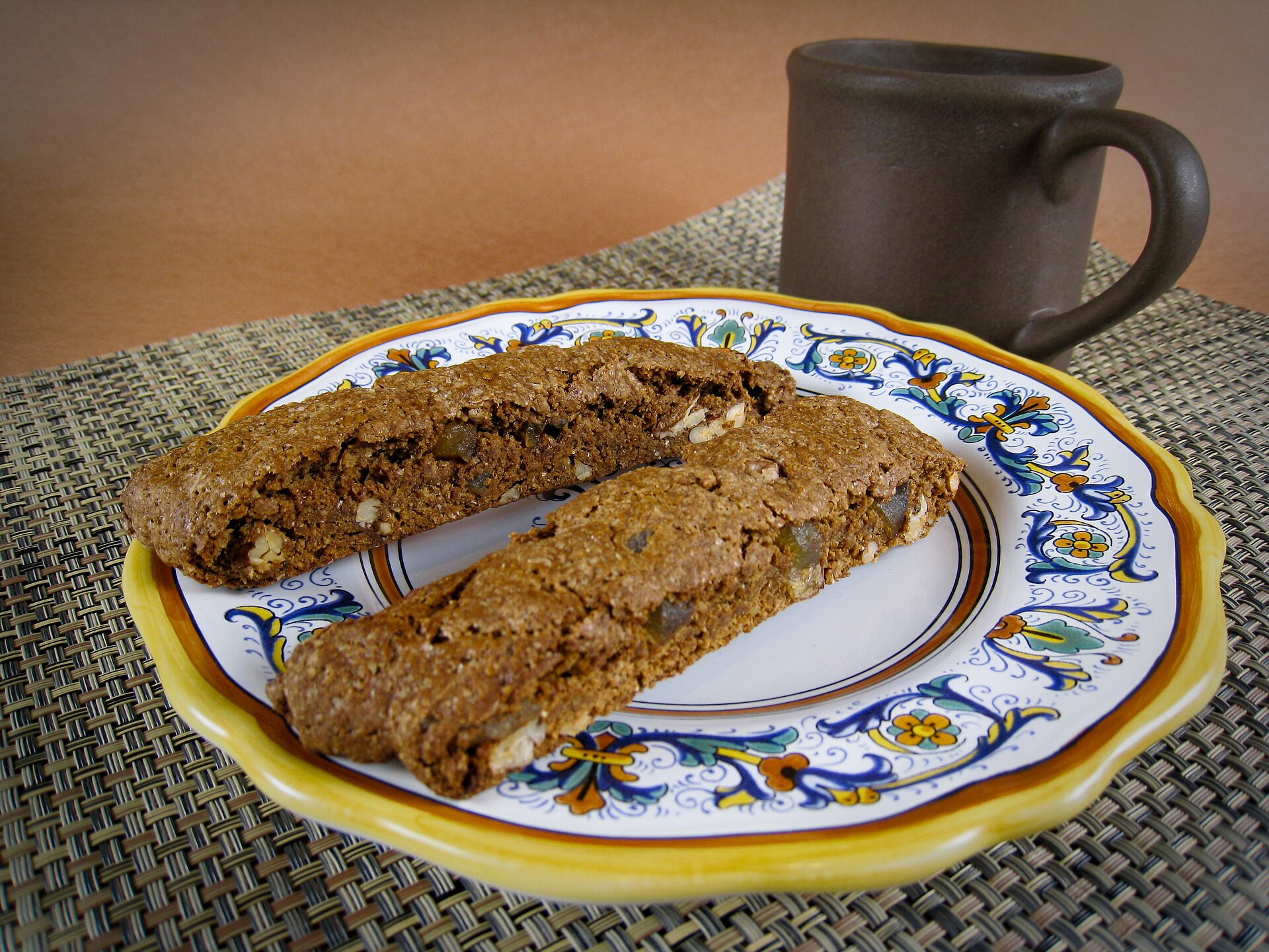 Gingerbread pecan biscotti on a patterned plate with a mug