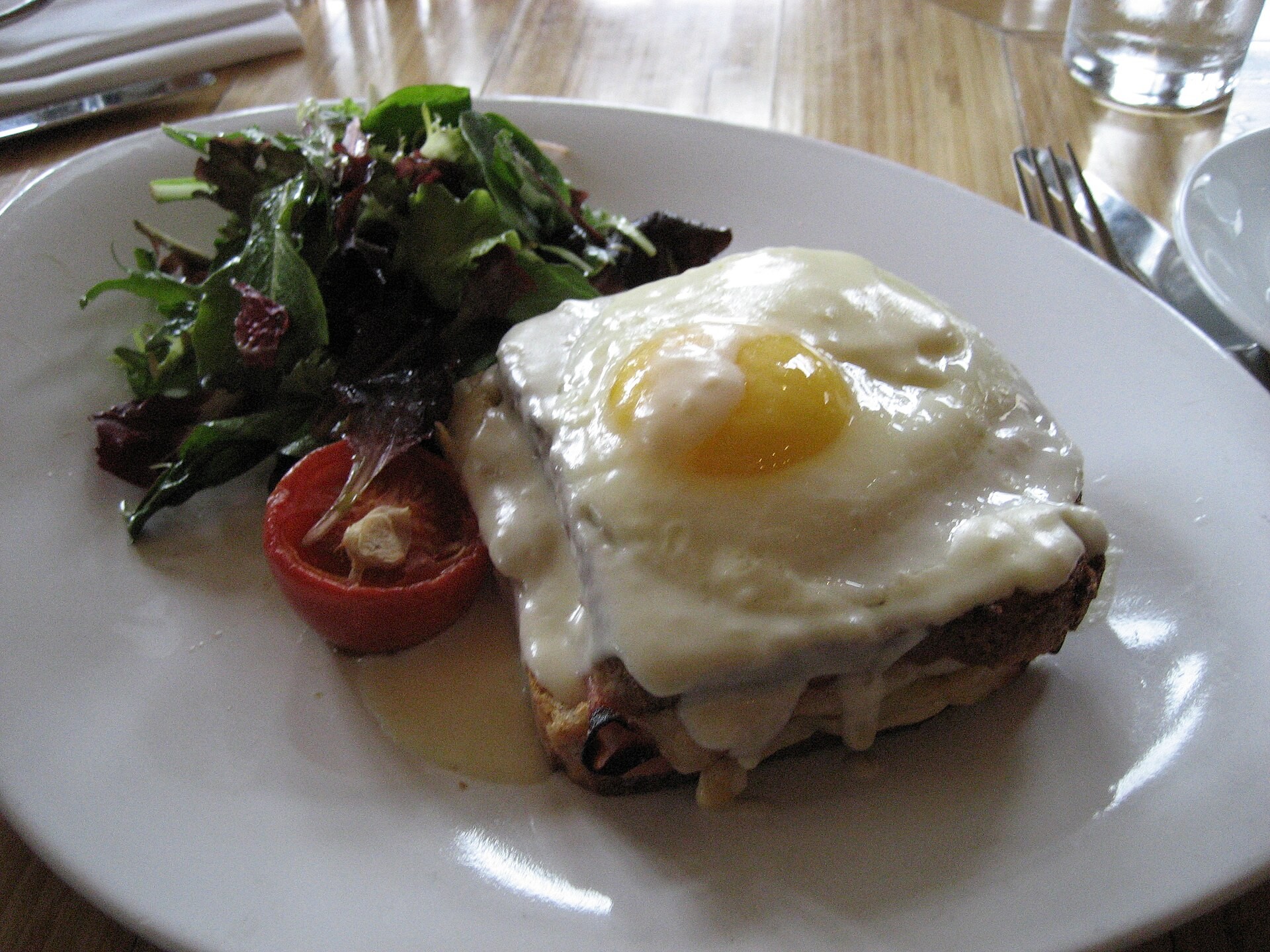 Croque madame topped with a fried egg beside a green salad