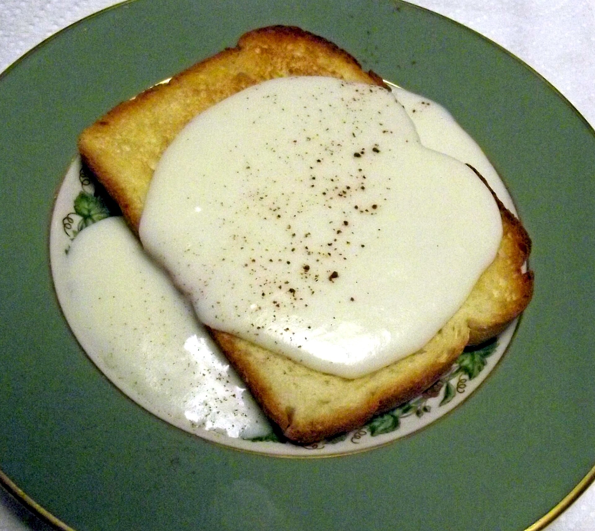 Milk toast with creamy white sauce and black pepper on a green plate