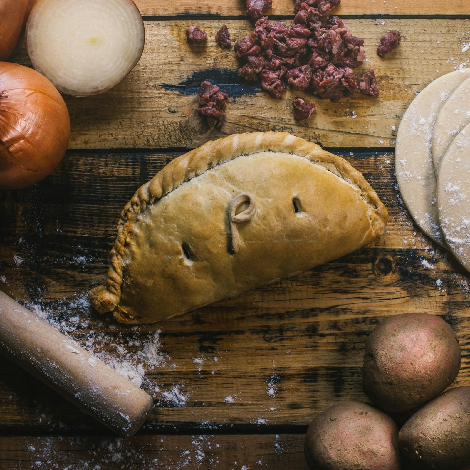 Golden crimped pasty hand pie on a floured wooden board