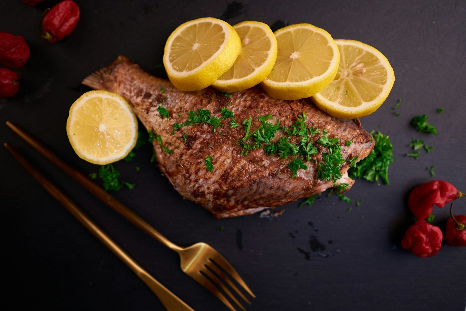 Grilled fish fillet with lemon slices and herbs on a dark plate