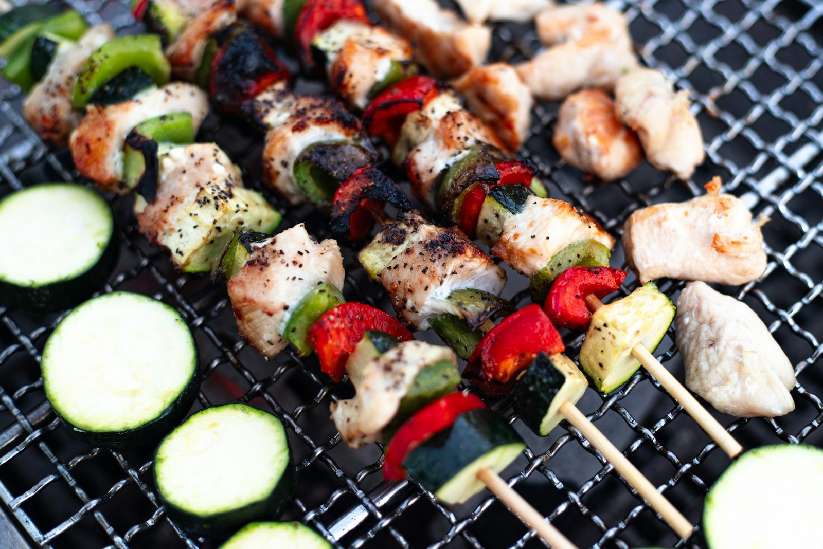 Chicken and vegetable skewers on a grill next to zucchini slices