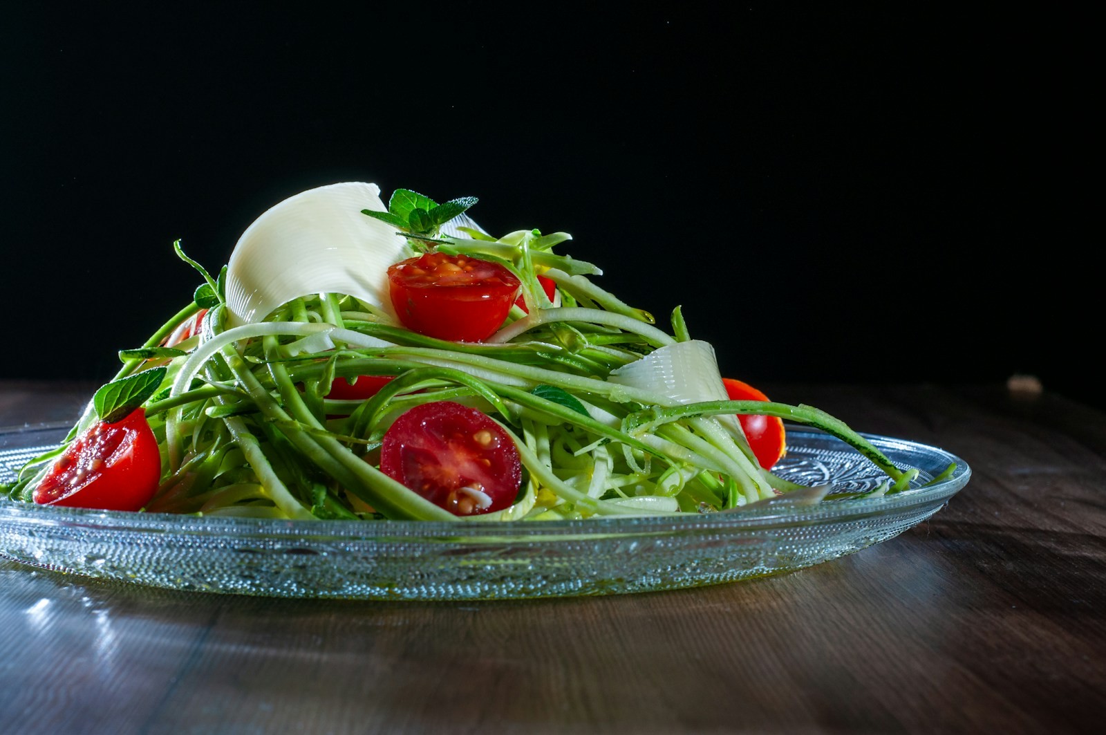 Raw zucchini noodles with cherry tomatoes and mozzarella on a glass plate