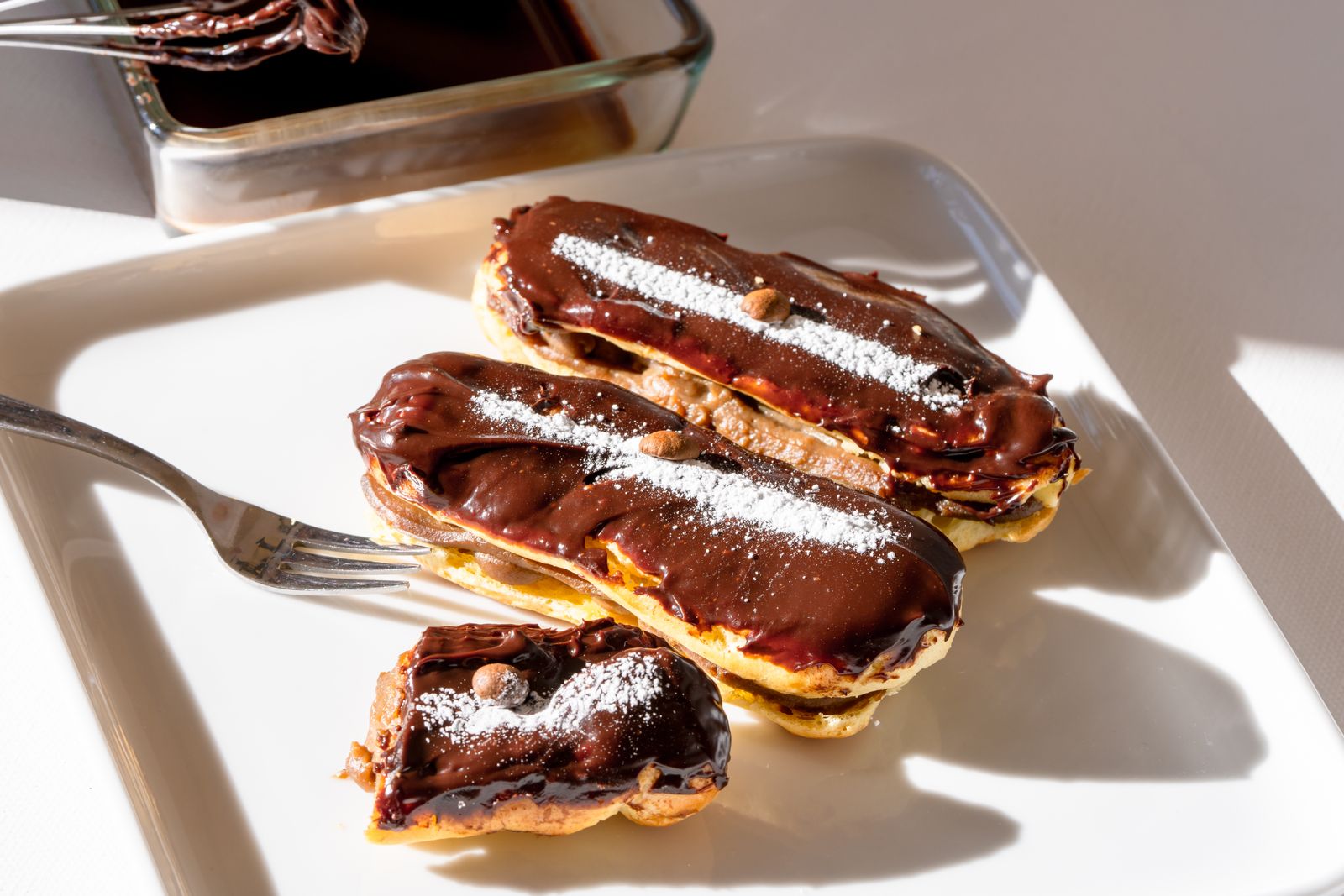 Homemade chocolate eclairs with glossy icing on a white plate