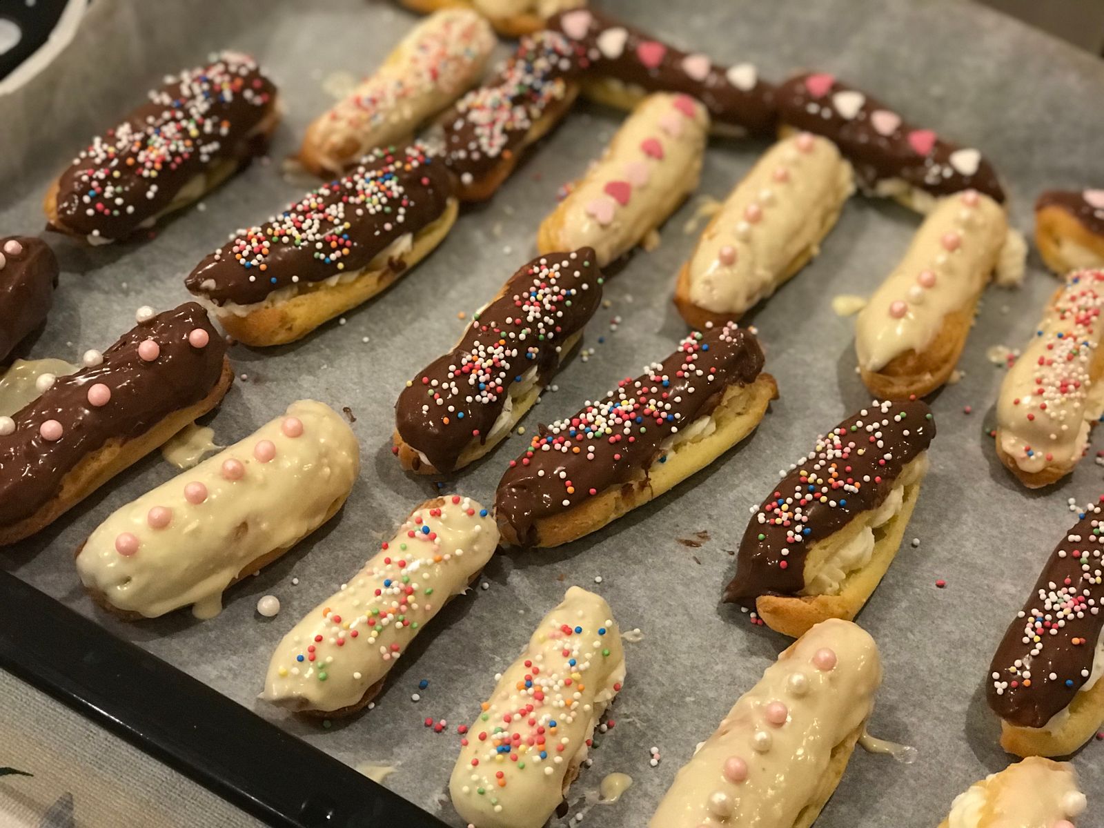 Mini eclairs with chocolate and sprinkles on a baking tray