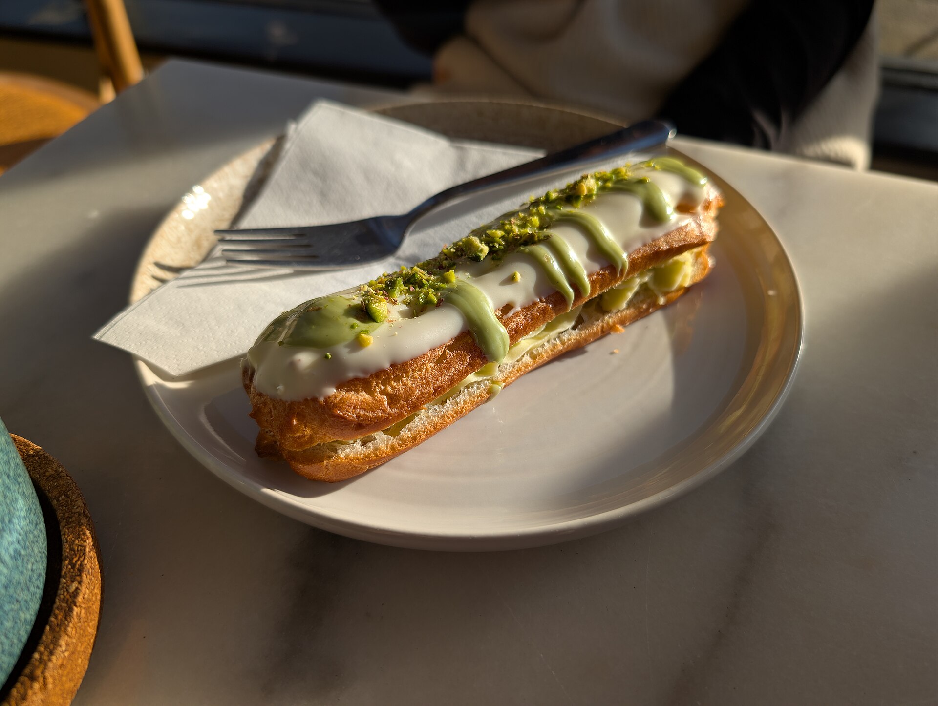 A pistachio eclair with white glaze and chopped pistachios