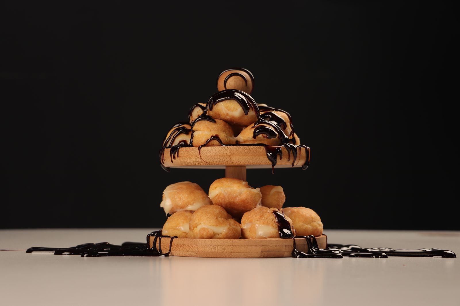 Profiteroles stacked on a wooden stand with chocolate sauce