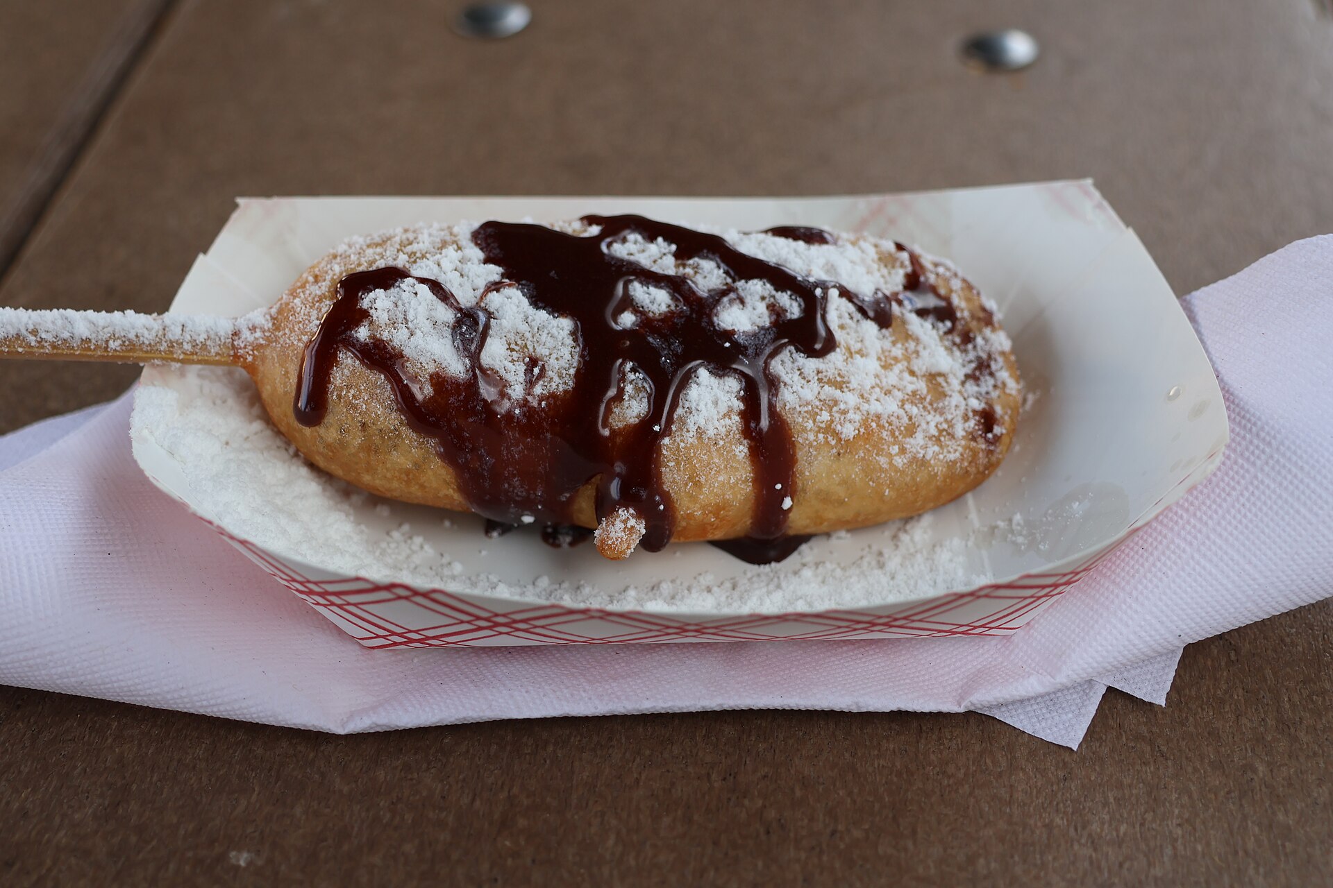 A deep fried chocolate bar on a stick with chocolate drizzle and powdered sugar