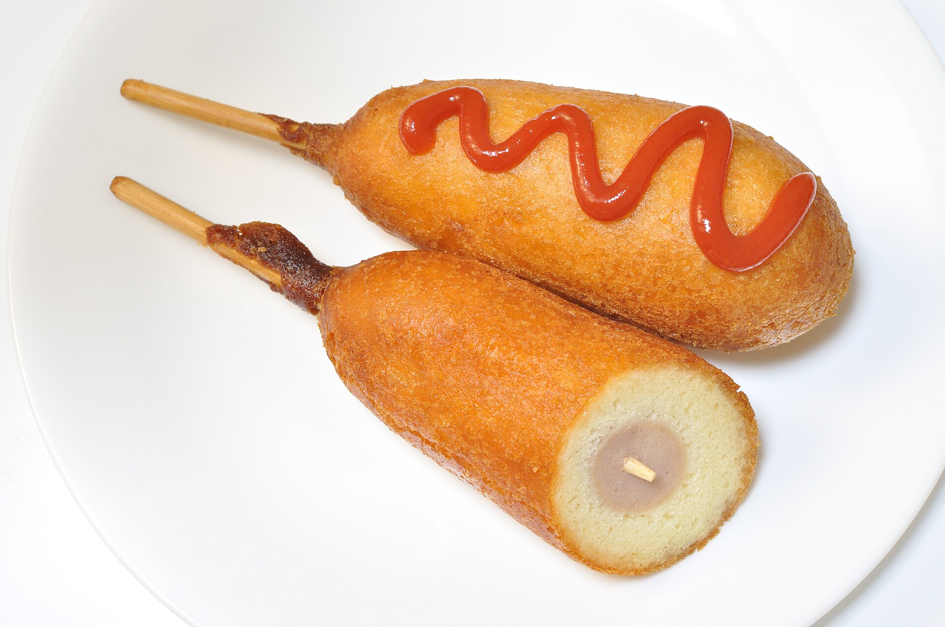 Two golden corn dogs on sticks with a ketchup swirl