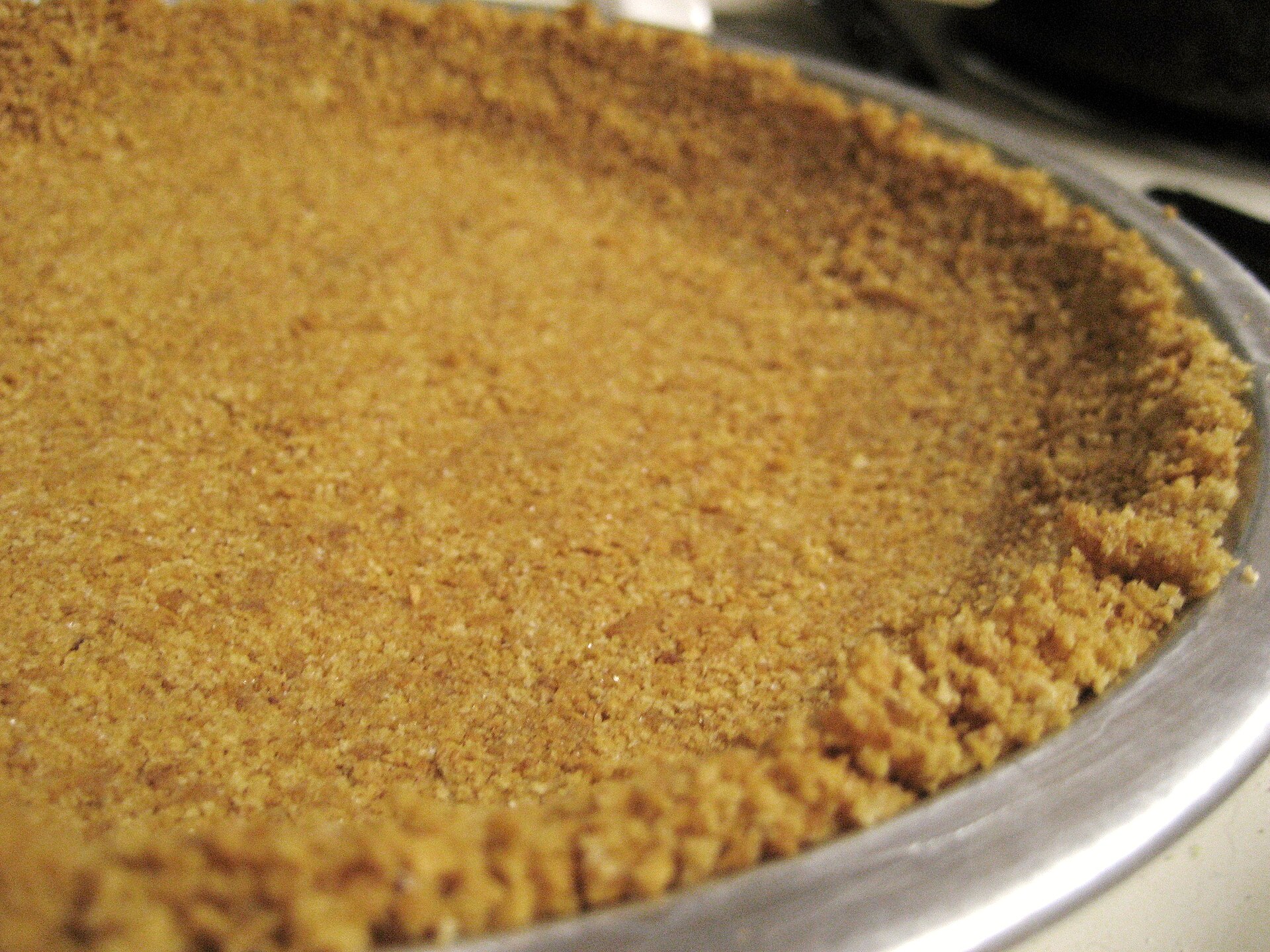 A golden homemade graham cracker crust in a pie plate