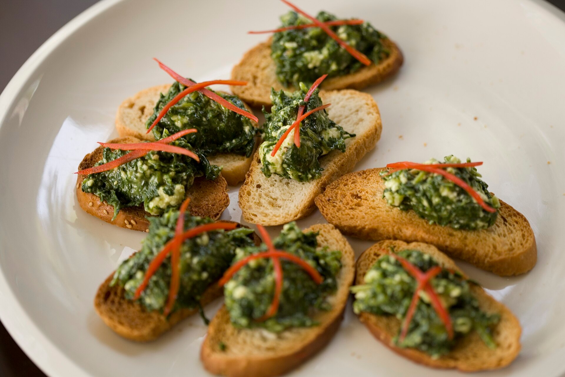 Basil pesto crostini with thin red pepper strips
