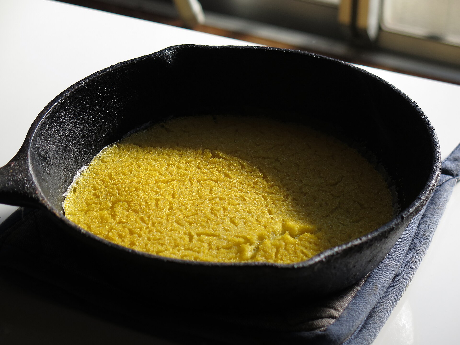 Cornmeal hoecake cooking in a cast iron skillet