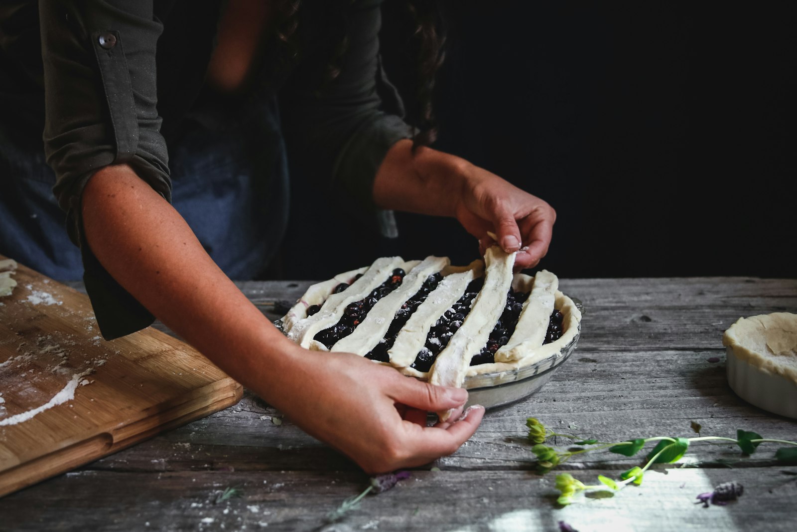 Hands weaving pastry strips into a lattice pie crust design