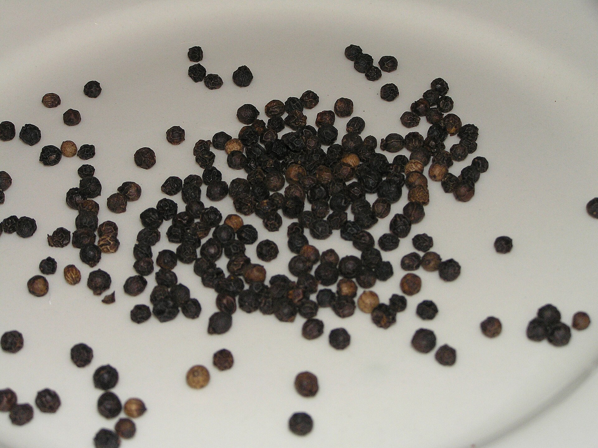 Whole black peppercorns on a white plate, ready to crack