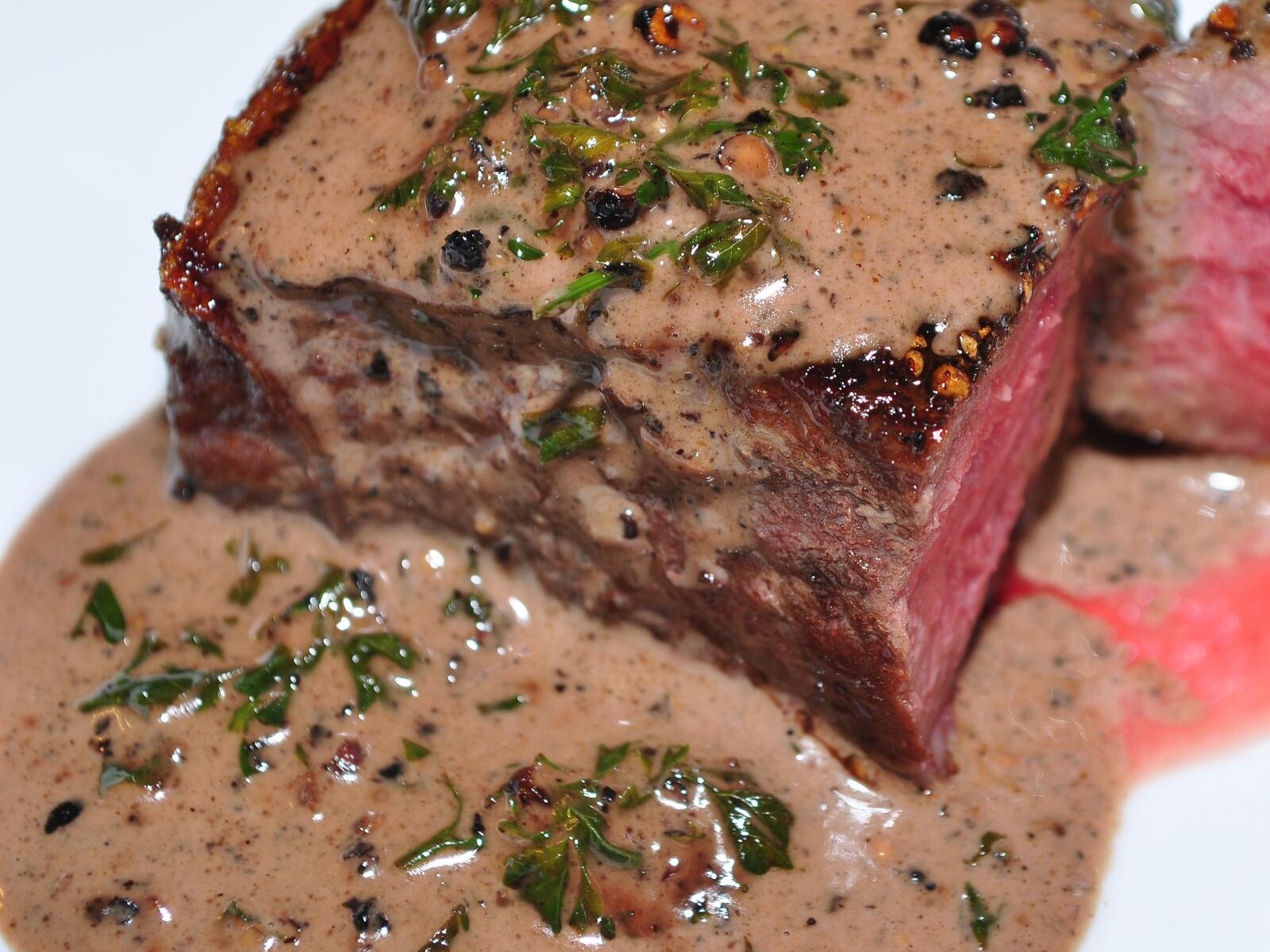 Sliced steak au poivre with pink centers and creamy peppercorn sauce
