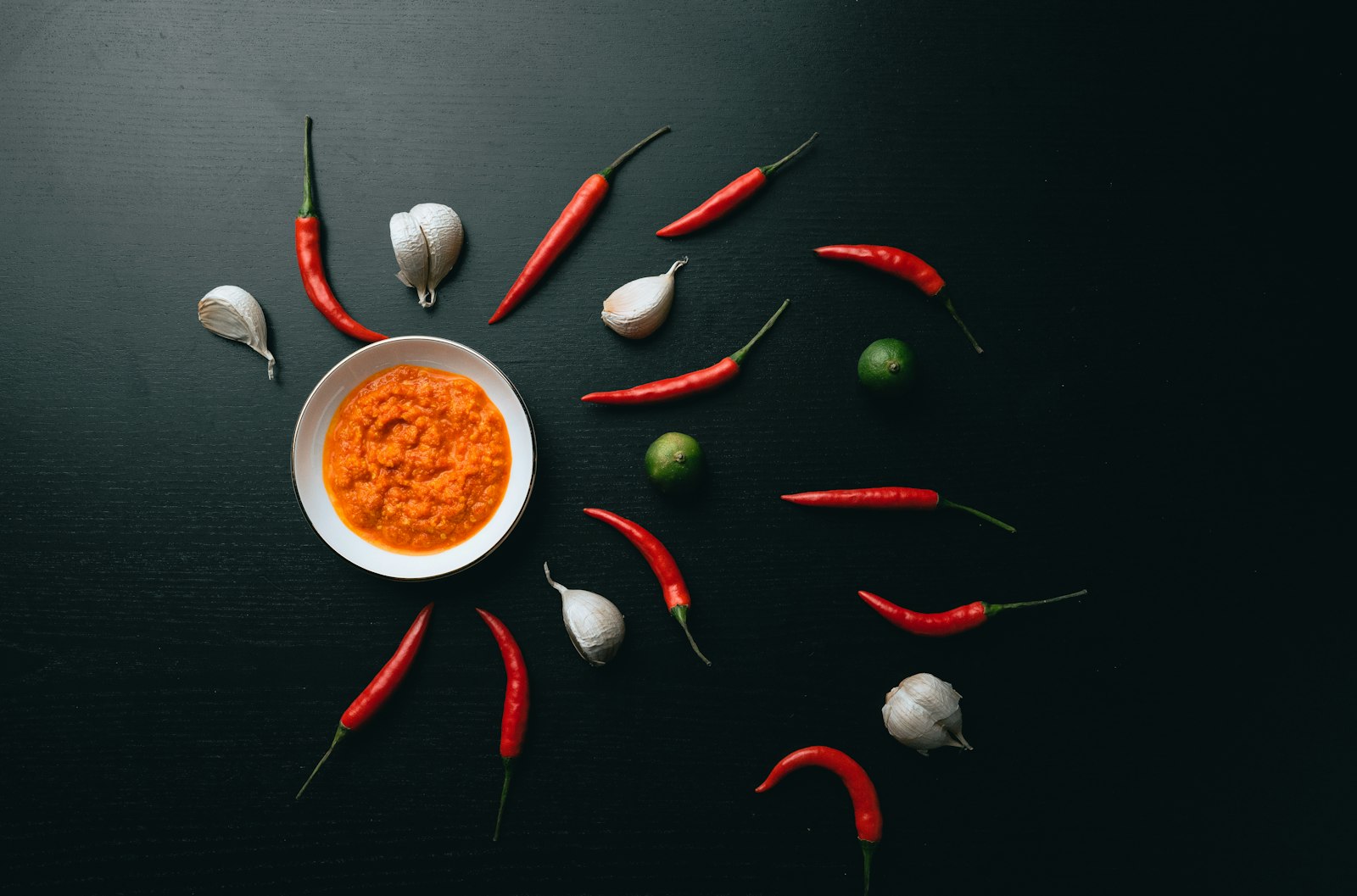 Small bowl of chili sauce surrounded by red chilies and garlic