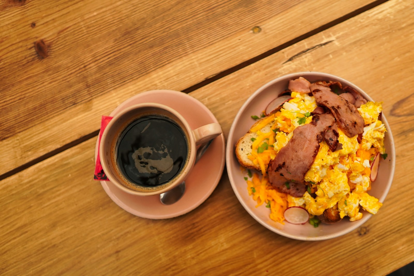 Breakfast bowl with scrambled eggs, bacon and cheese next to coffee