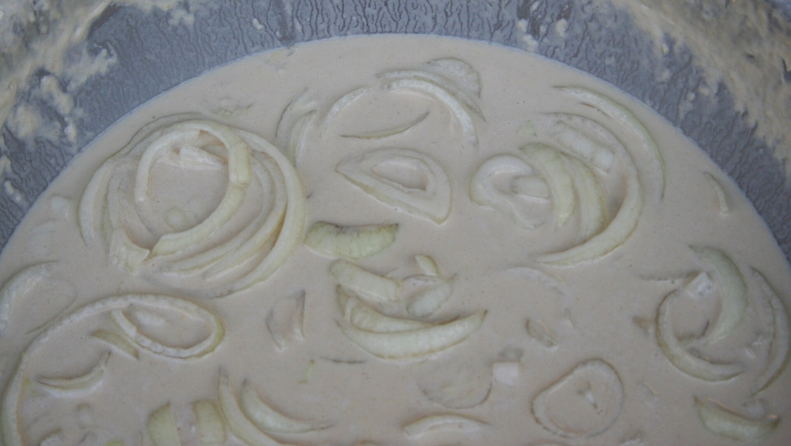 Sliced onion rings soaking in a creamy buttermilk batter