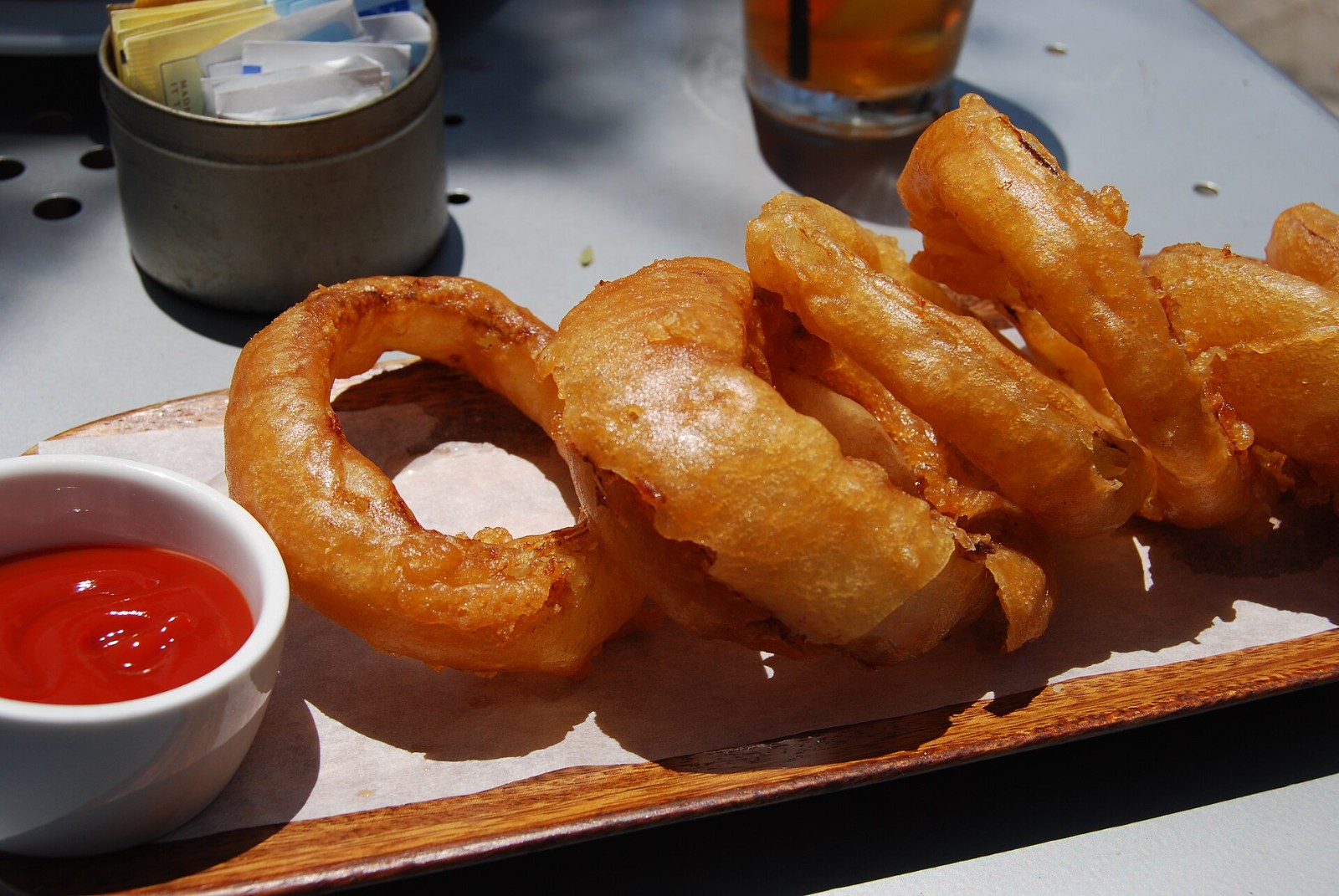 Golden beer-batter onion rings on a wooden tray with ketchup