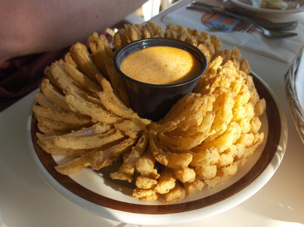 Fried blooming onion opened like a flower with a cup of spicy dip in the center