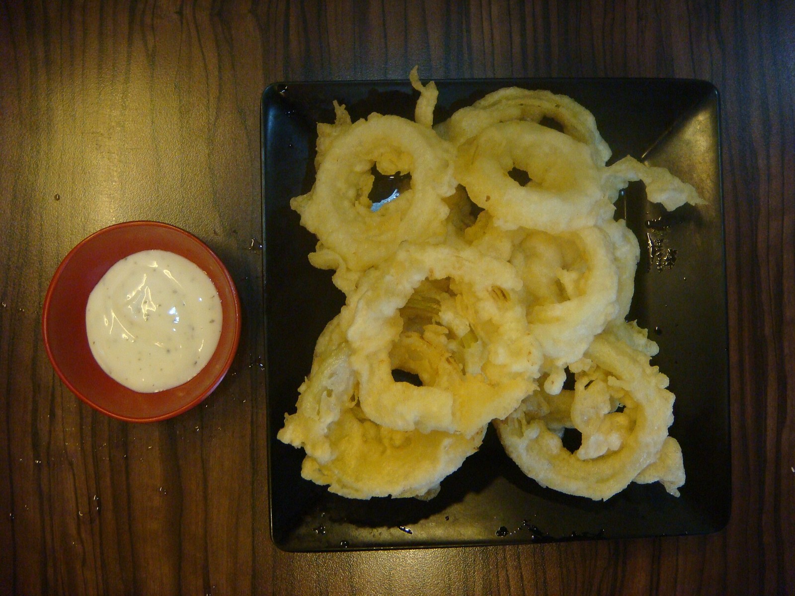 Fried onion rings on a black plate with a creamy dipping sauce for blooming onion recipes