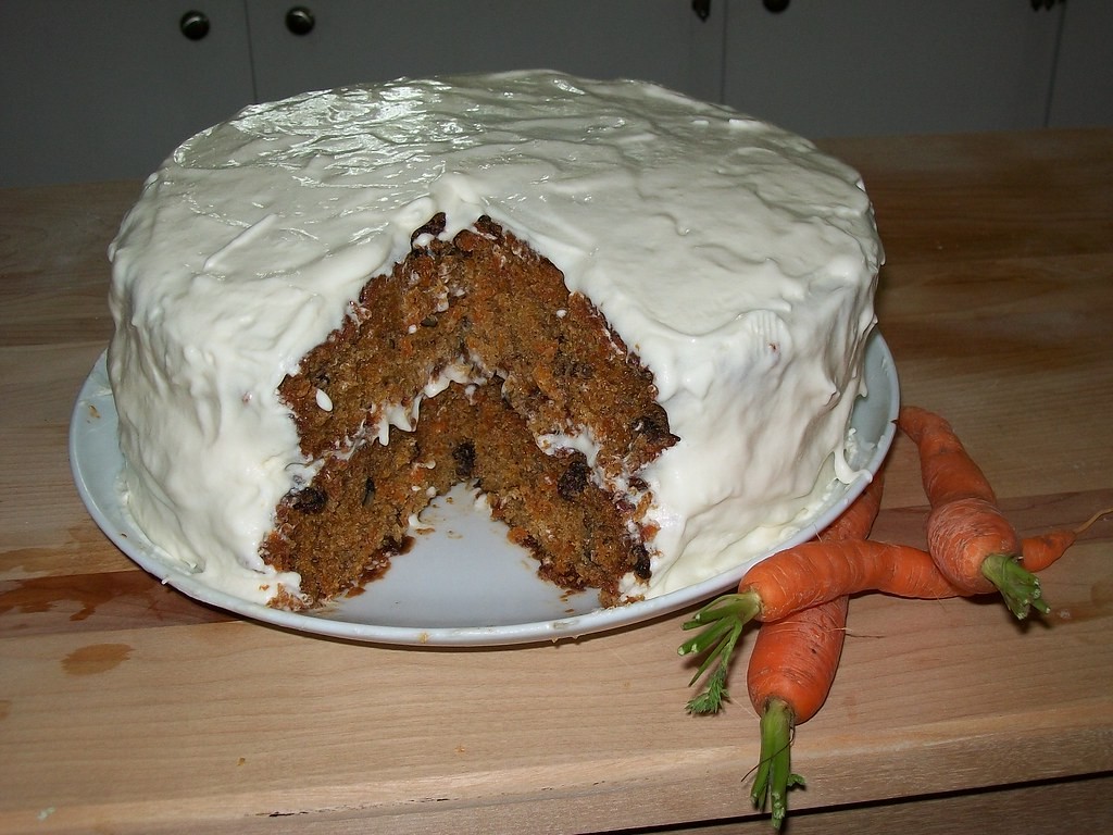 Classic two-layer carrot cake with white cream cheese frosting, a slice cut out, fresh carrots beside it