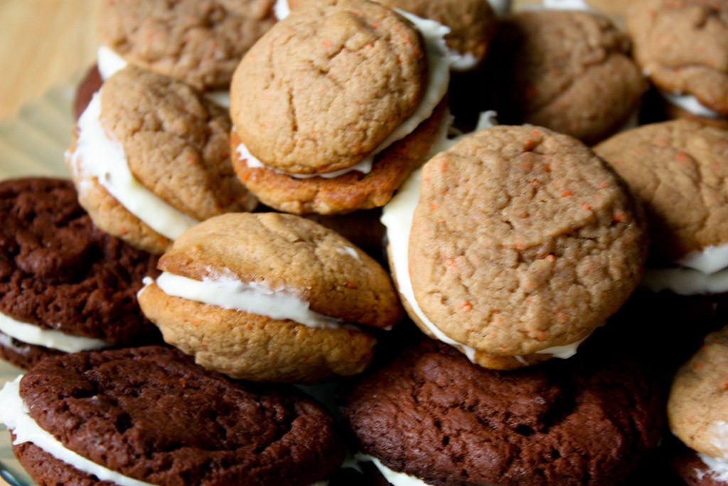 Carrot cake sandwich cookies filled with cream cheese frosting piled on a plate