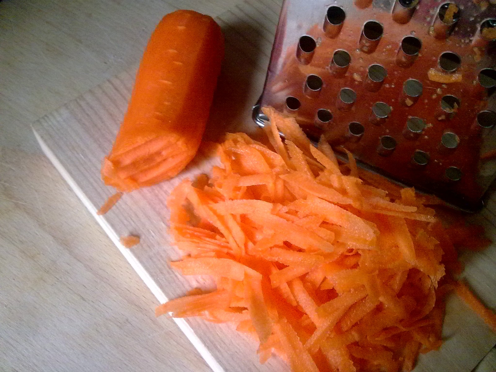 Finely grated carrots next to a box grater and a whole carrot
